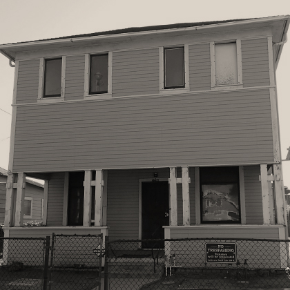 The Harada House with a no trespassing sign and chain link fencing. One second floor porch window is boarded up.