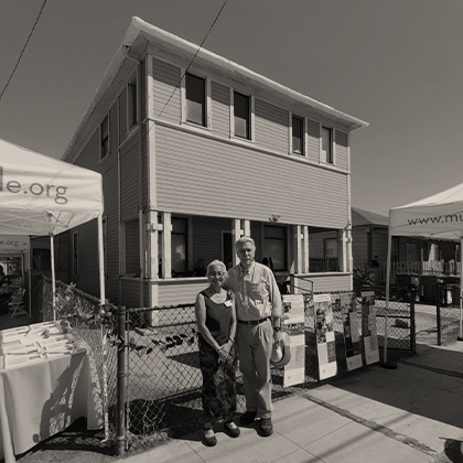 Craig Swan and Naomi Harada stand in front of the Harada House, next to a Museum of Riverside popup tent, lemon garlands, and interpretive panels.