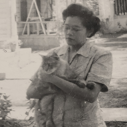 Sumi Harada stands on the Lemon Street sidewalk holding a cat. She is wearing a skirt suit and heels.