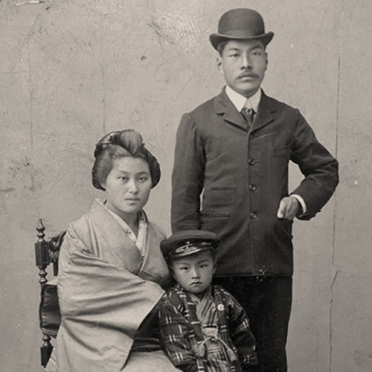 Portrait of Ken Harada with her husband Jukichi and son Masa Atsu, taken in Japan. Ken and Masa Atsu are dressed in traditional Japanese clothing, with Masa Atsu also wearing a US military hat. Jukichi is wearing a dark bowler hat and suit.