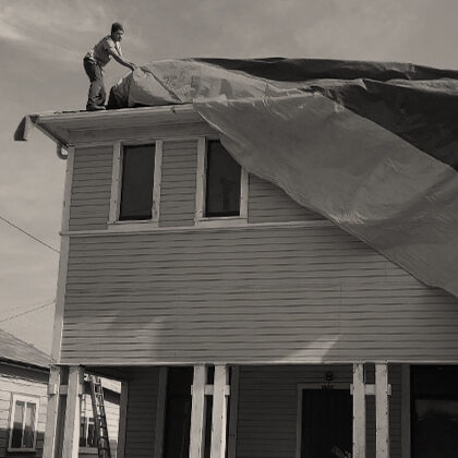 Two men placing a bright yellow and blue fumigation tent over the roof of the Harada House.